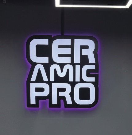 어두운 실내 벽에 설치된 흰색 글자와 보라색 후광의 CERAMIC PRO 로고